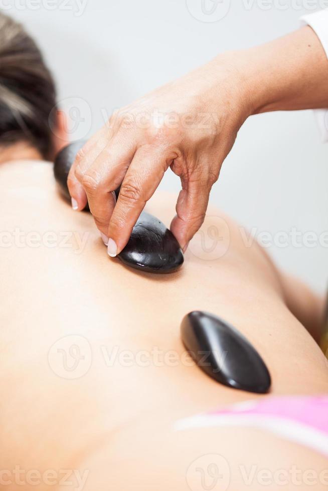 Doctor performing a hot volcanic stones therapy on a young female patient back photo