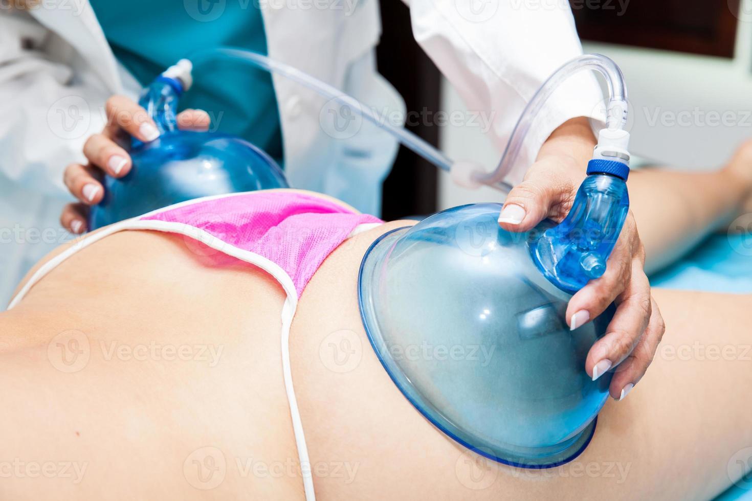 Doctor performing a vacuum therapy treatment for buttocks lifting on a young female patient photo