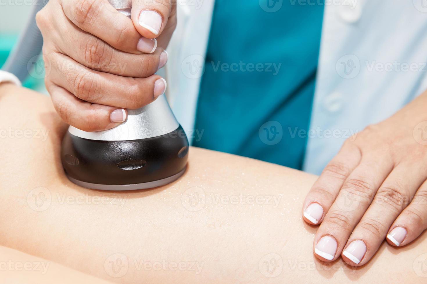 Doctor performing an  ultracavitation treatment on a young female patient leg photo