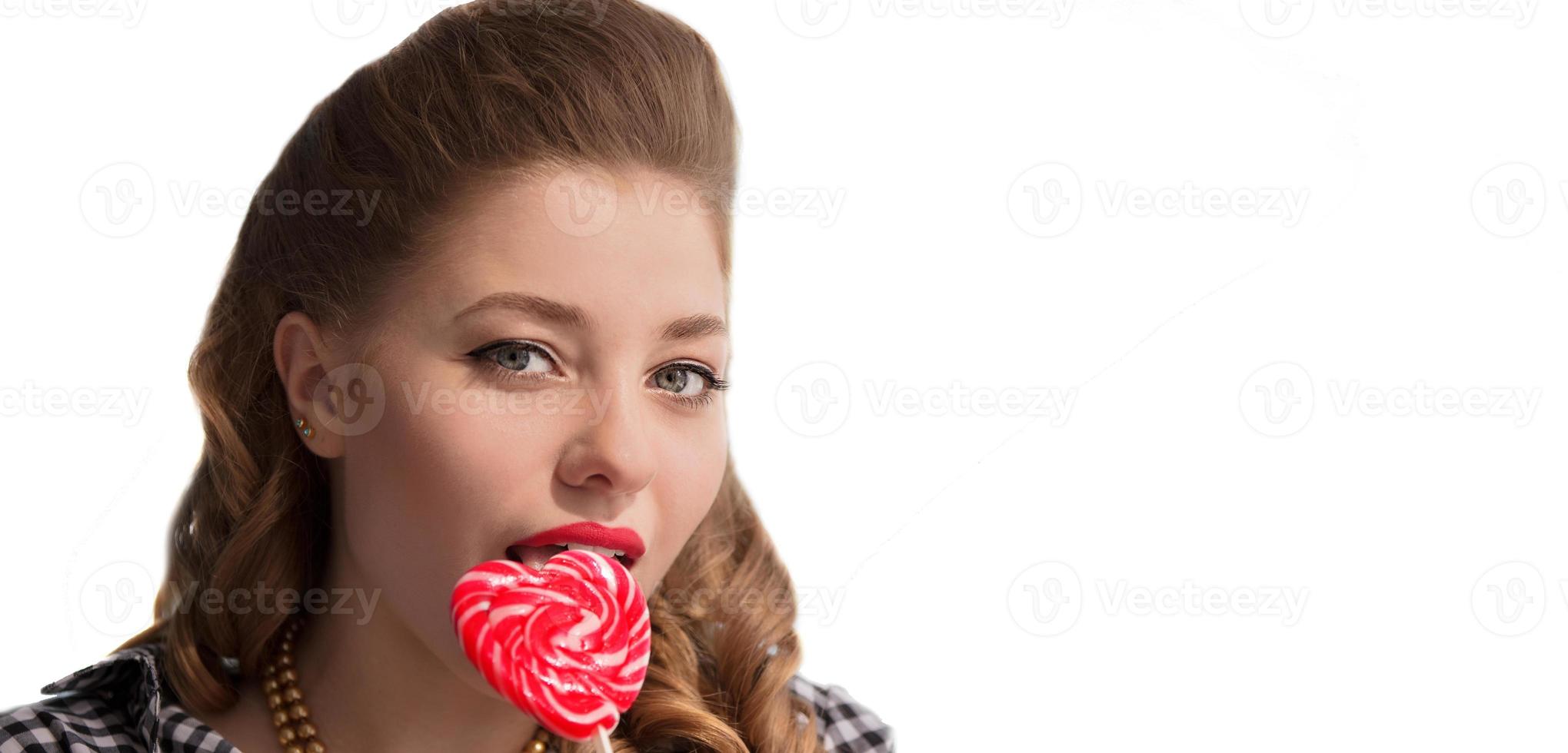 The face of a girl with candy on a stick in the form of a heart on a white background. Sweet woman. photo