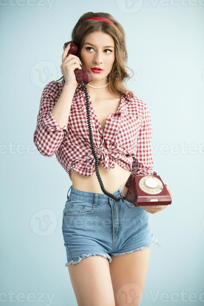 mujer en el estilo de el cincuenta joven retro mujer en mezclilla pantalones cortos con un antiguo teléfono. foto