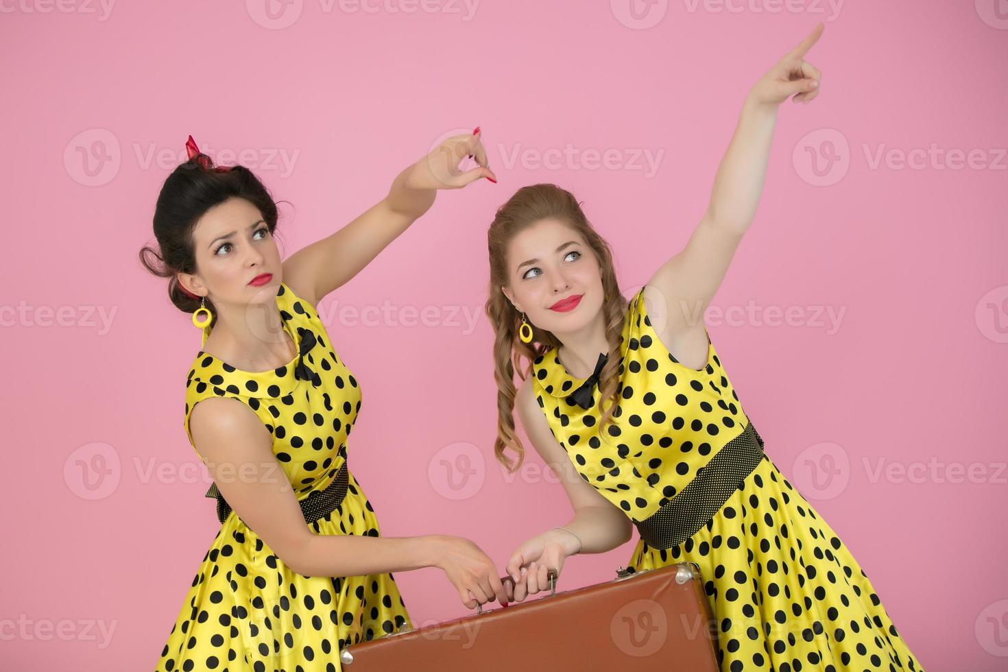 retro viajero muchachas con maleta. dos mujer vestido en cincuenta estilo son participación un antiguo maleta. foto