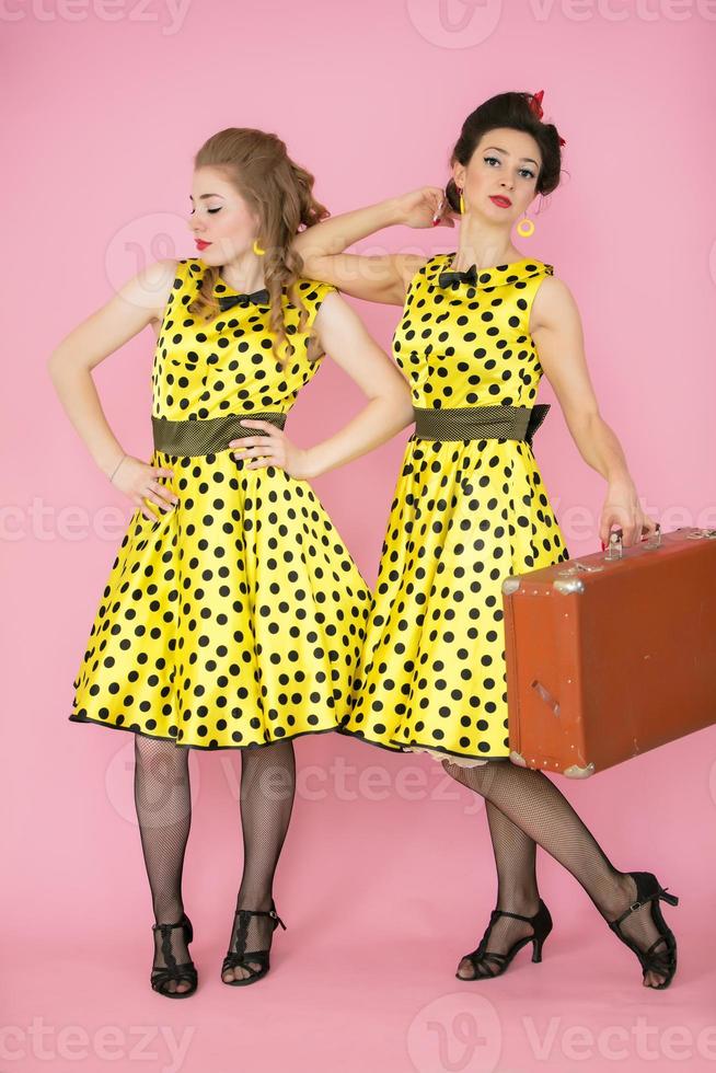 Retro girls with a suitcase. Two women in yellow dresses on a pink background. photo