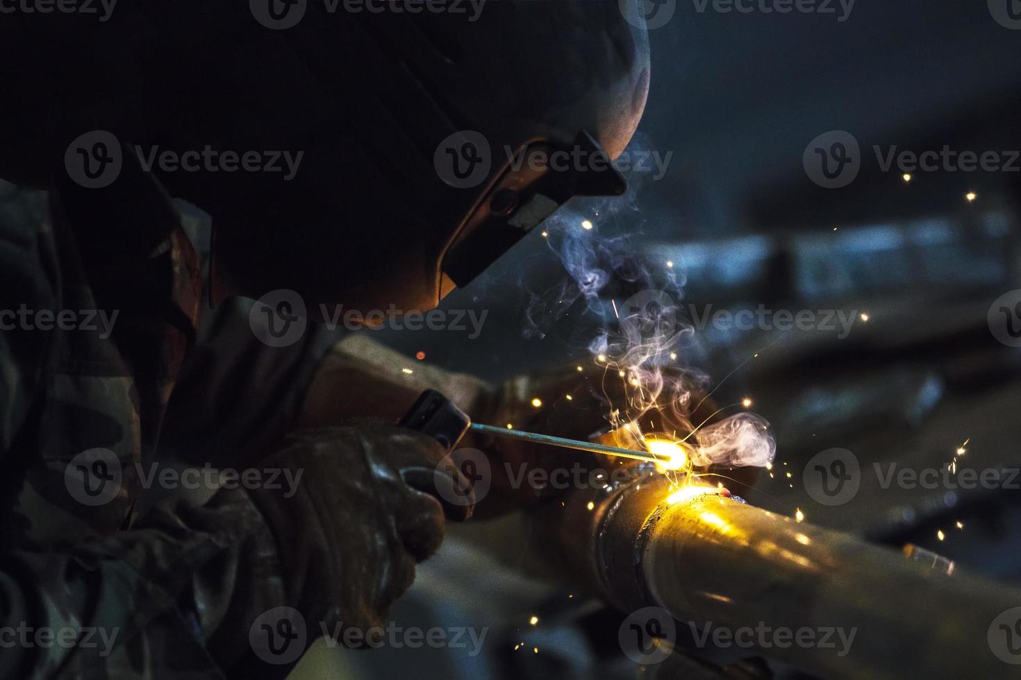 Welder at work. Man in a protective mask. The welder makes seams on the metal. Sparks and smoke when welding. photo
