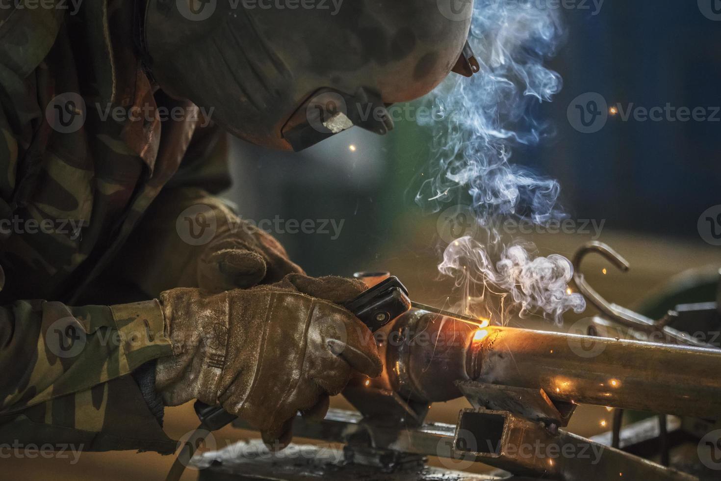 Welder at work. Man in a protective mask. The welder makes seams on the metal. Sparks and smoke when welding. photo