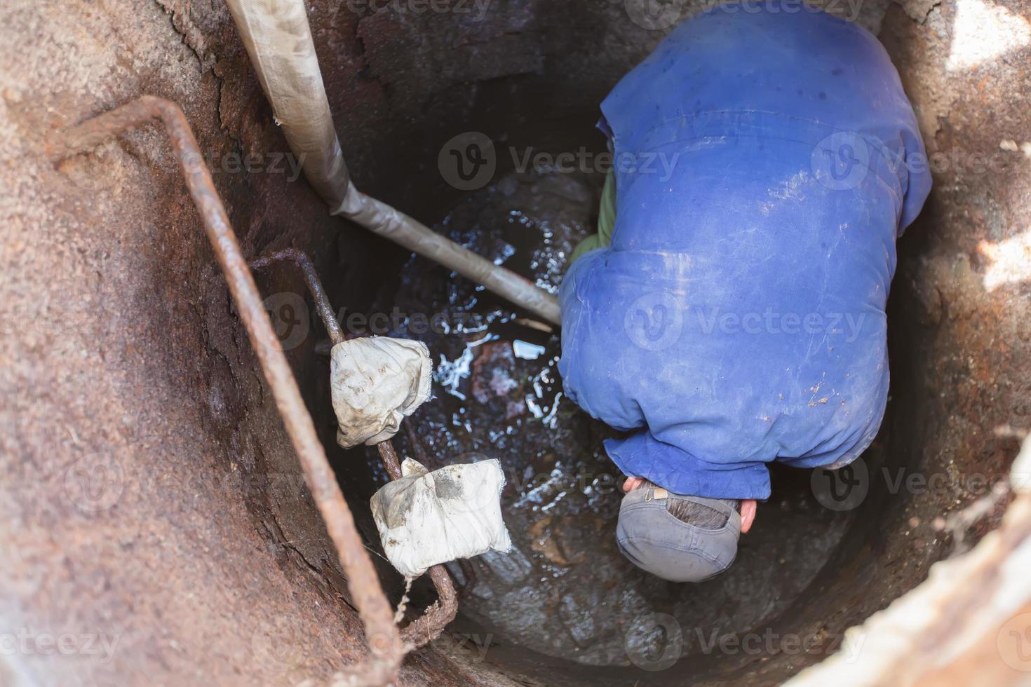 Worker cleans the sewer hatch.A worker cleans a sewer hatch. A man in the hatch. photo