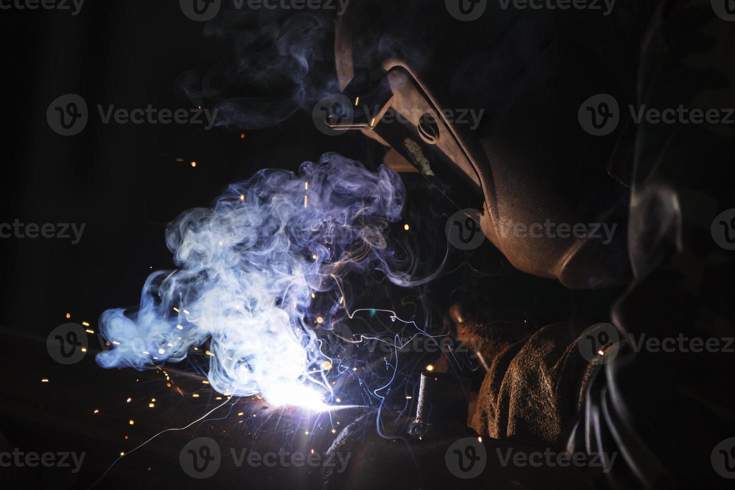 Welder at work. Man in a protective mask. The welder makes seams on the metal. Sparks and smoke when welding. photo