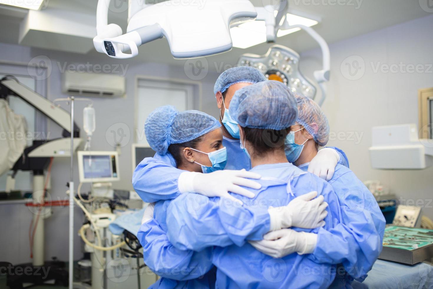 Partial view of hard-working male and female hospital team in full protective wear standing together in group embrace photo