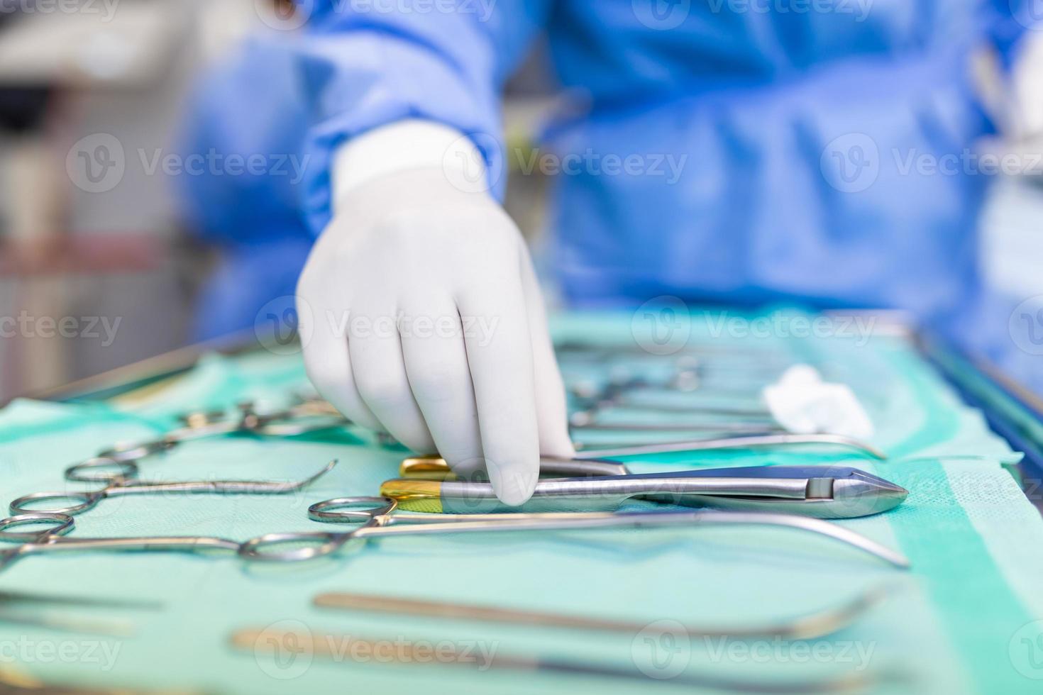 Nurse hand taking surgical instrument for group of surgeons at background operating patient in surgical theatre. Steel medical instruments ready to be used. Surgery and emergency concept photo