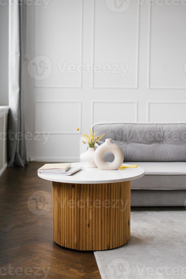 Interior of a modern living room with a gray sofa and a coffee table near the window with a vase with mimosa photo