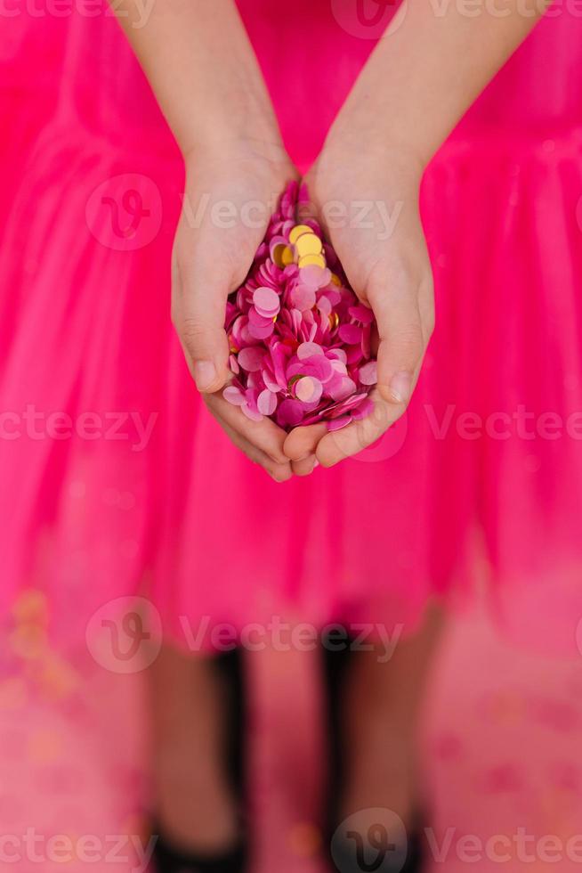 Bright pink and gold paper confetti in the palms of a birthday girl in a dress at a party photo