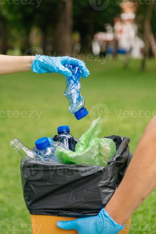 personas mano participación basura botella el plastico y vaso poniendo dentro reciclar bolsa. el plastico concepto. foto