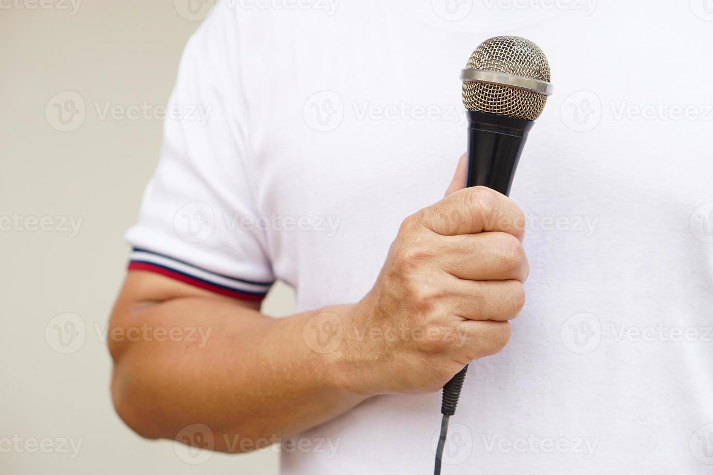 hombre sostiene y hablar o canta en micrófono. concepto, herramienta o dispositivo tecnología ese traduce sonido vibraciones en el aire dentro electrónico señales a altoparlante para entretenimiento o público discurso. foto