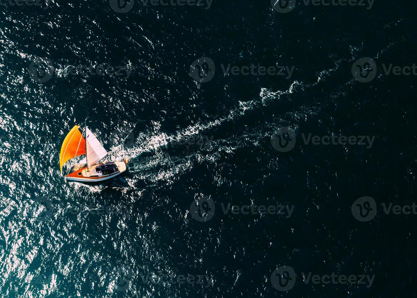 Aerial drone top down photo of a sailboat with a bright orange mast against a deep blue ocean