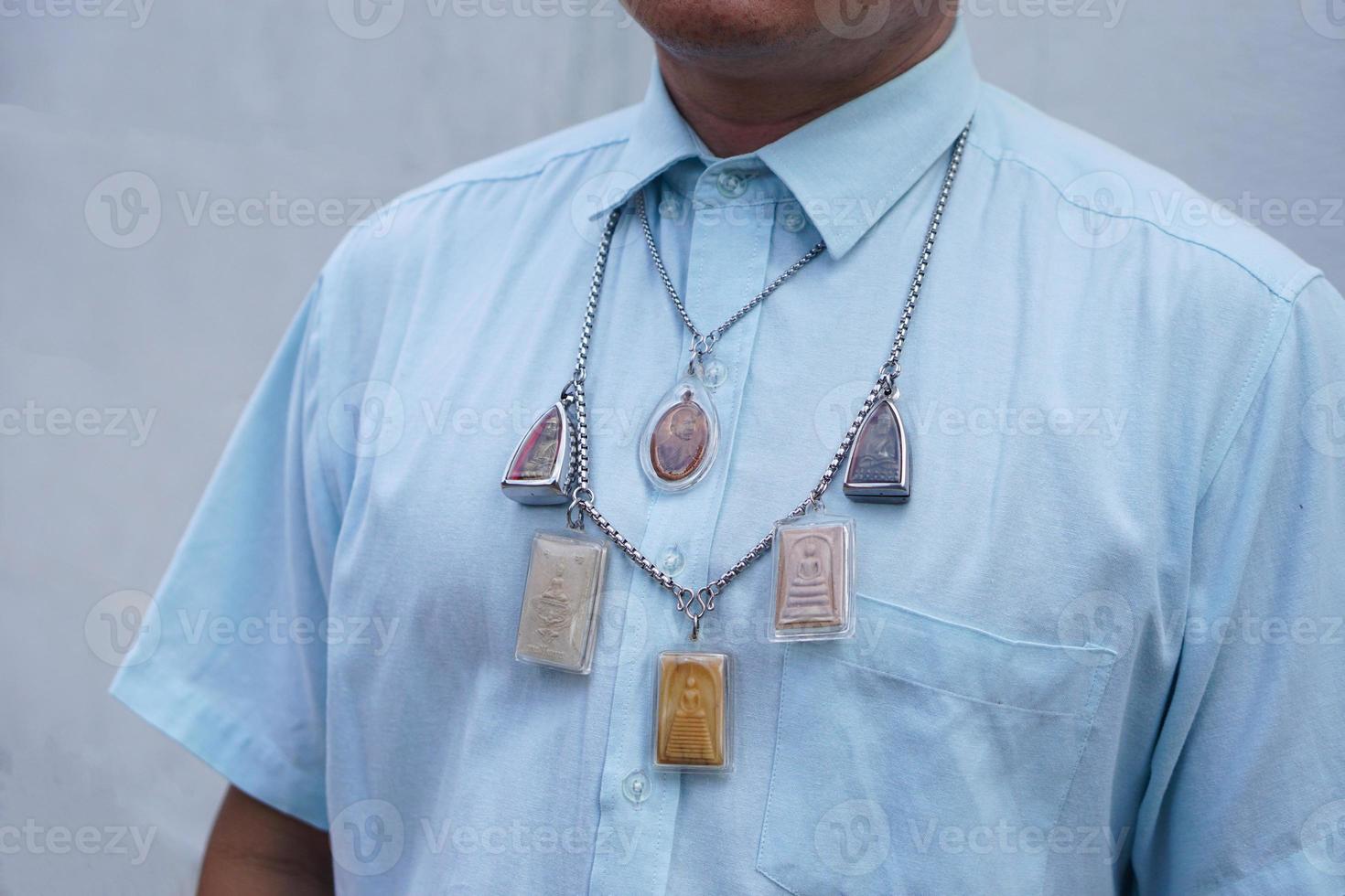Closeup man in blue shirt wear Thai Buddha amulet necklace. Concept, faith and belief of Buddhist for holy to protect from dangers, bring good luck, business prosperity and wealth. photo