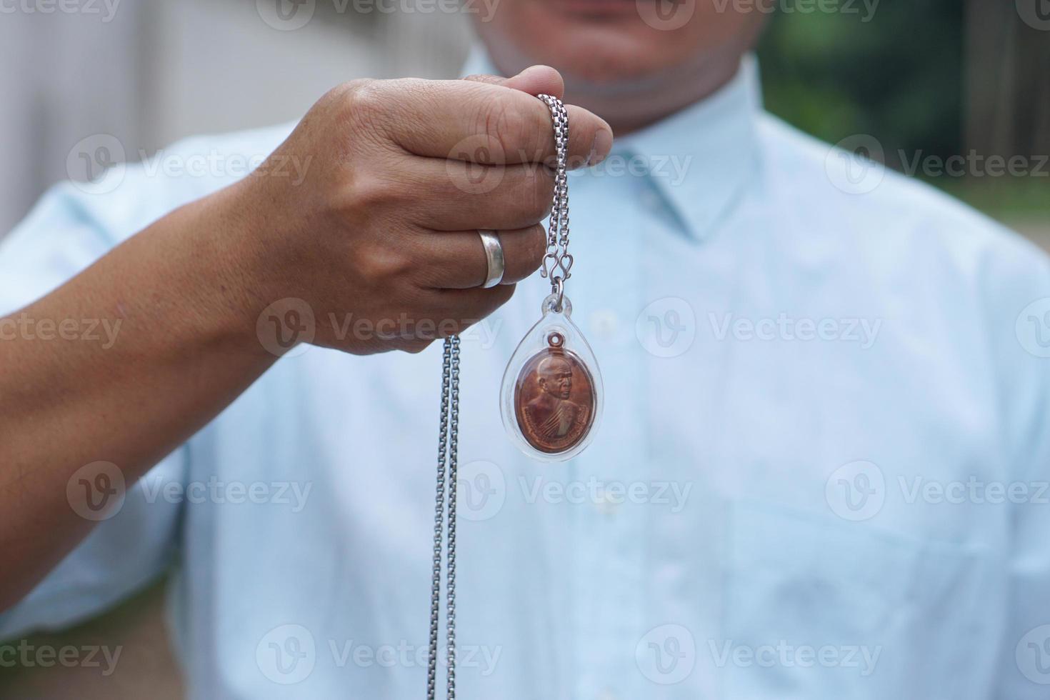 Closeup man in blue shirt holds Thai Buddha amulet necklace.  Concept, faith and belief of Buddhist for holy to protect from dangers, bring good luck, business prosperity and wealth. photo