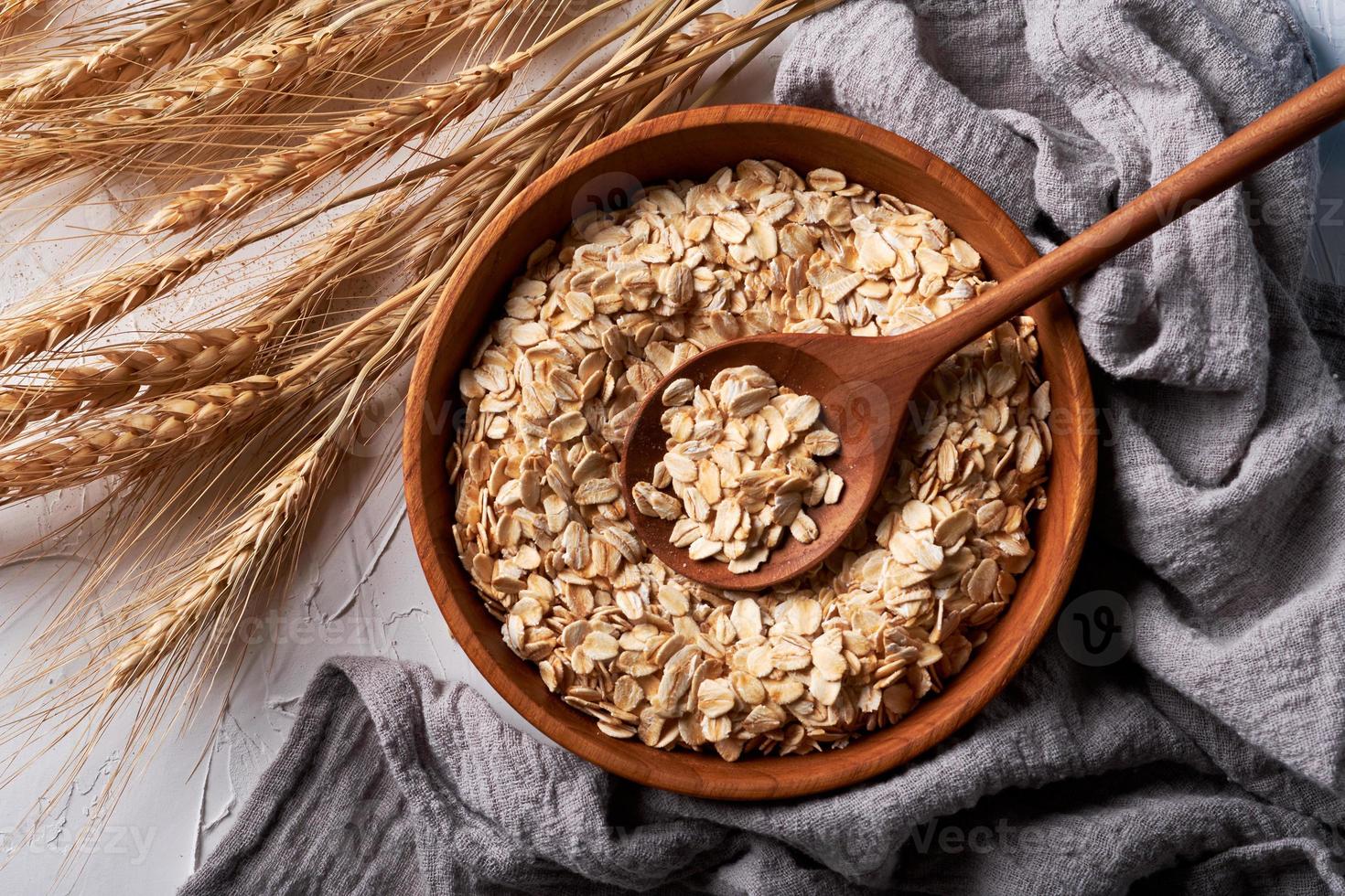 top view rolled oats or oat flakes in bowl with wooden spoon background photo