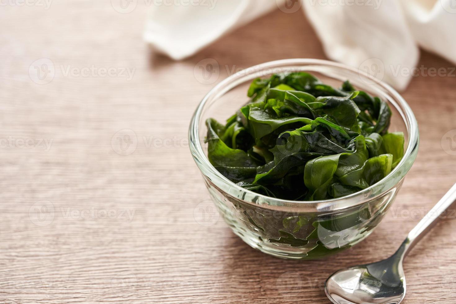 close up laminaria Kelp seaweed in glasses bowl and steel spoon on wooden table background with copy space photo
