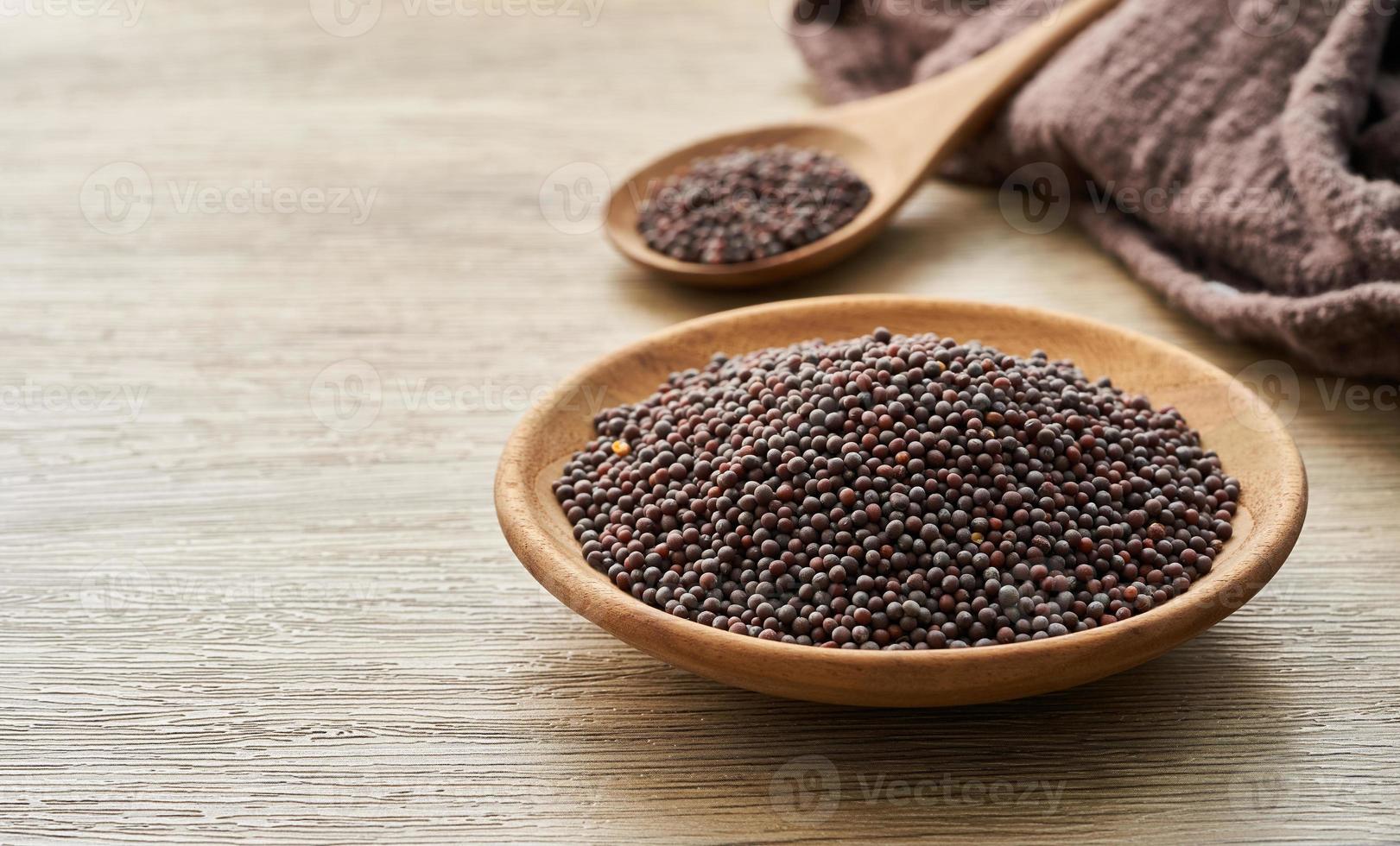 negro mostaza semilla en madera plato y cuchara en de madera mesa antecedentes. un pila de negro mostaza semilla en madera plato en de madera mesa antecedentes foto