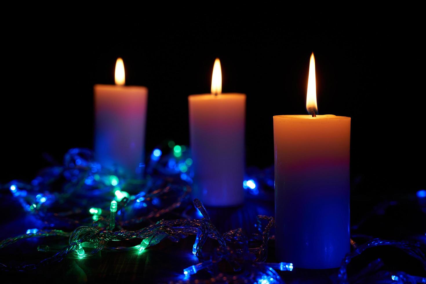 Flame candles with decorative lights on black table background photo