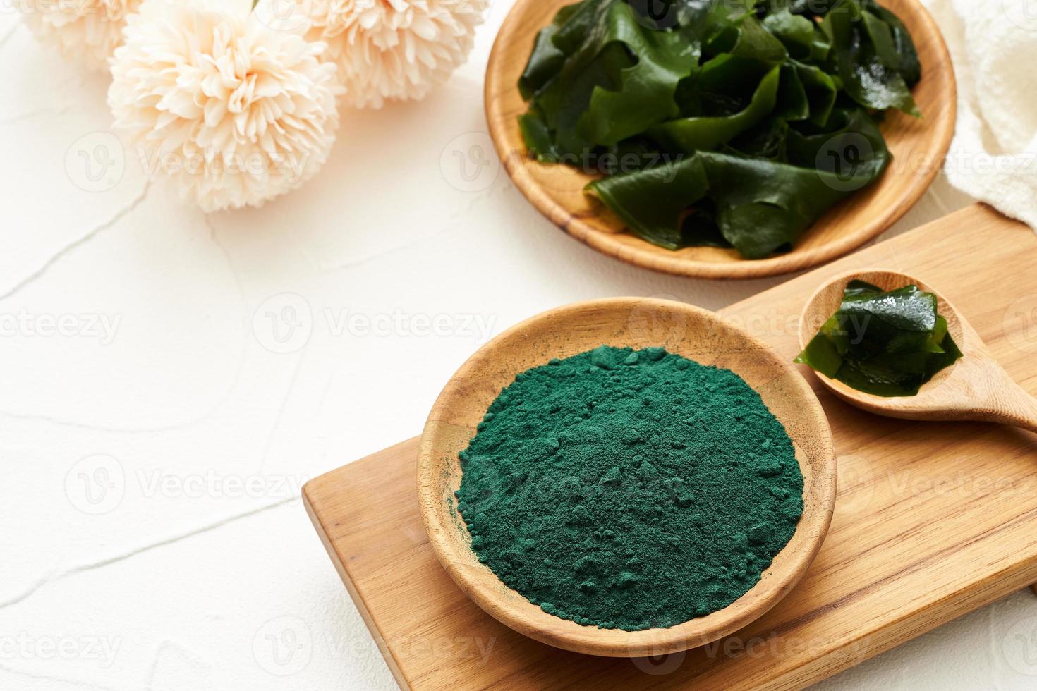 laminaria or kelp seaweed and spirulina powder in wood plate and spoon background. spirulina powder with konbu and alga food on white table background. photo