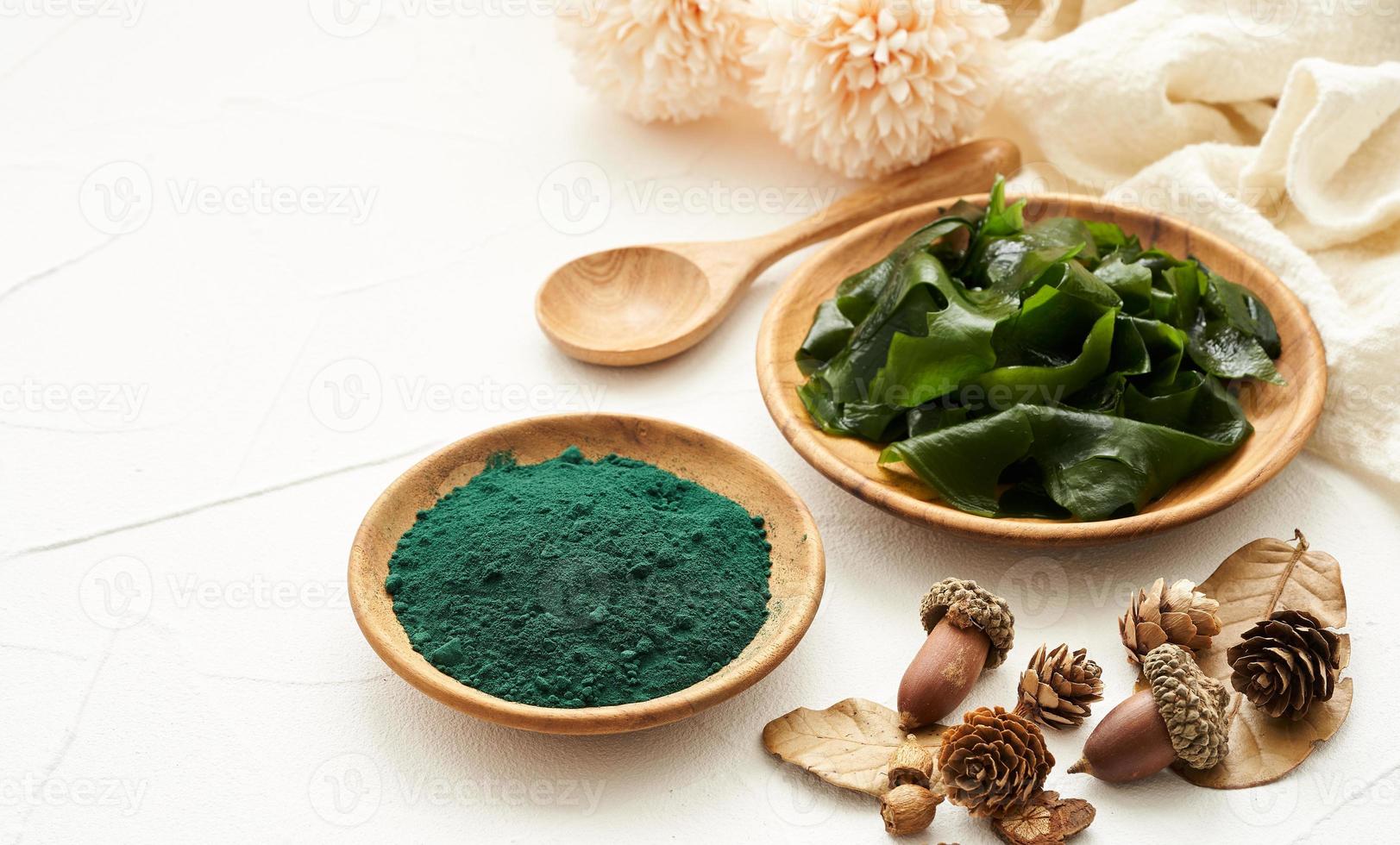 laminaria or kelp seaweed and spirulina powder in wood plate and spoon background. spirulina powder with konbu and alga food on white table background. photo