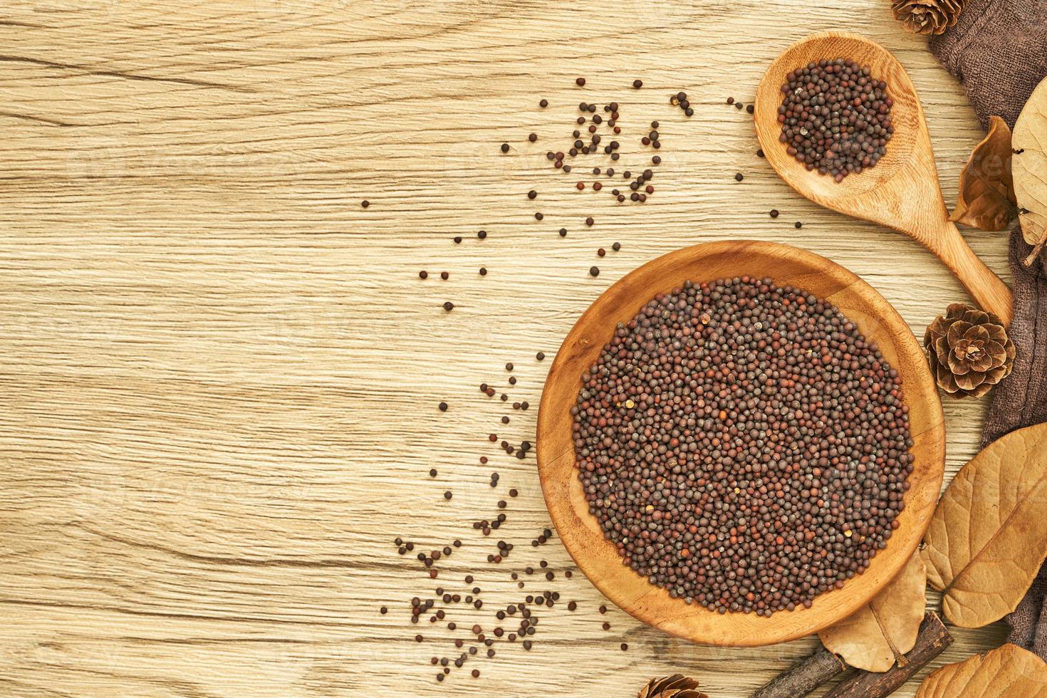 top view black mustard seed in wood plate and spoon on wooden table background. flat lay a pile of black mustard seed in wood plate on wooden table background. overhead photo