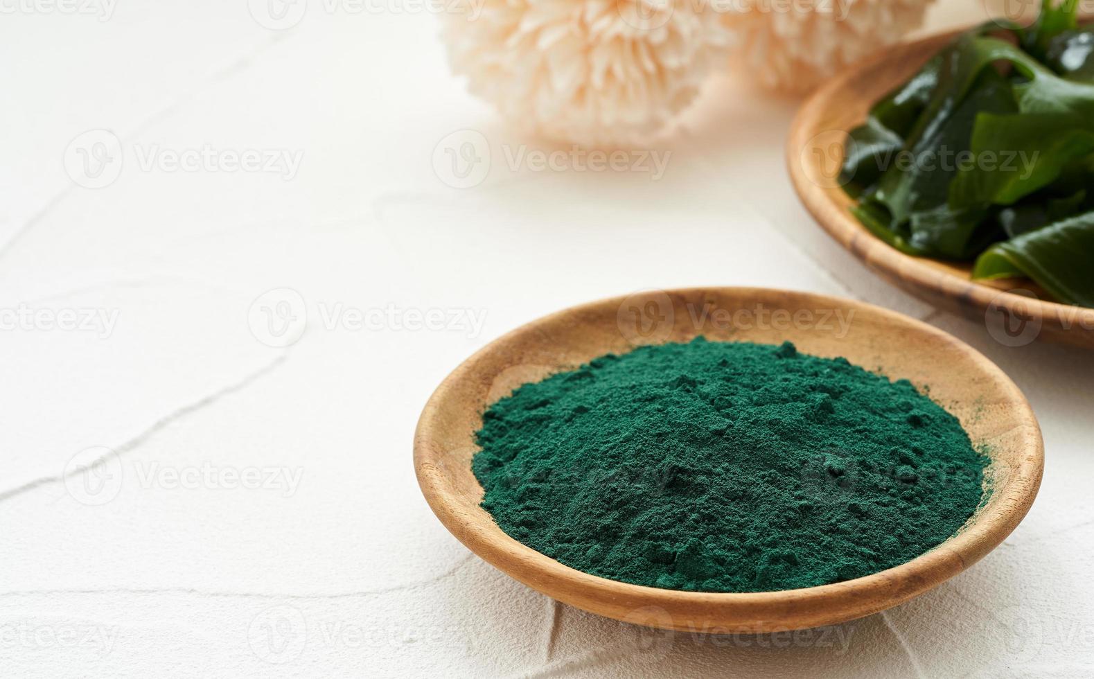 laminaria or kelp seaweed and spirulina powder in wood plate background. spirulina powder with konbu and alga food on white table background. photo