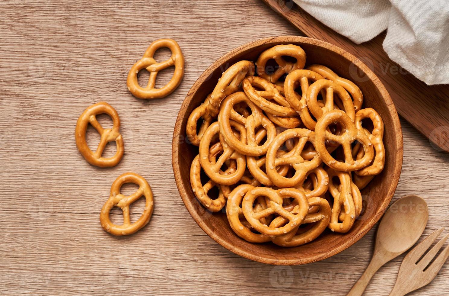 top view or flat lay mini salted pretzel in a wooden bowl with a spoon and fork on wood table overhead background. photo