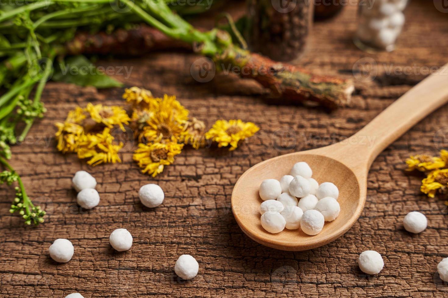 concept of homeopathic pills in a wooden spoon and bottles with herb on wooden table background photo