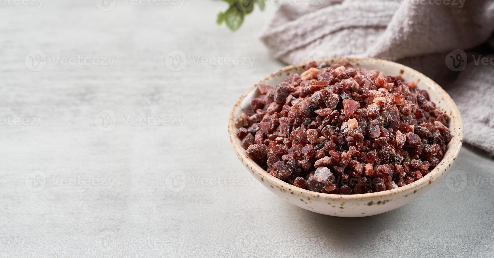 Himalayan black salt in a ceramic bowl with the wooden scoop on white cement texture background with copy space photo