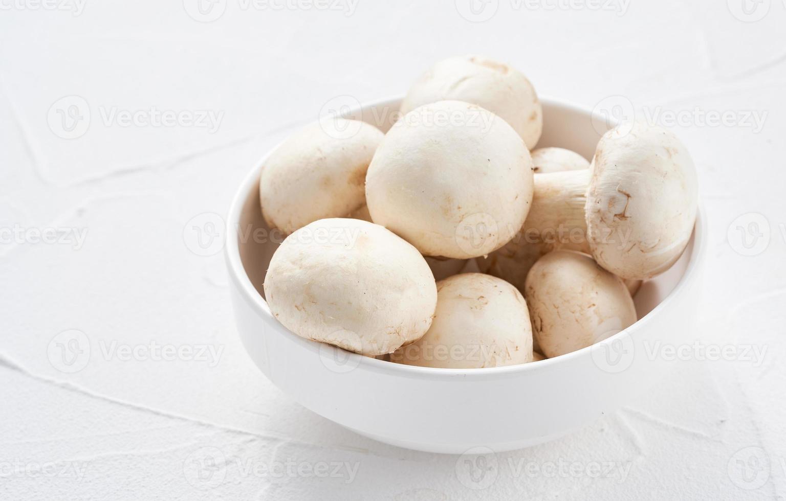 white champignon button mushroom in bowl on white table background. pile of white champignon button mushroom. group of champignon button mushroom photo