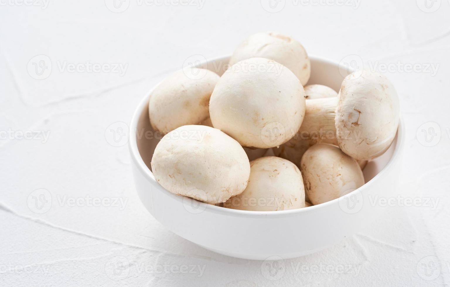 white champignon button mushroom in bowl on white table background. pile of white champignon button mushroom. group of champignon button mushroom photo