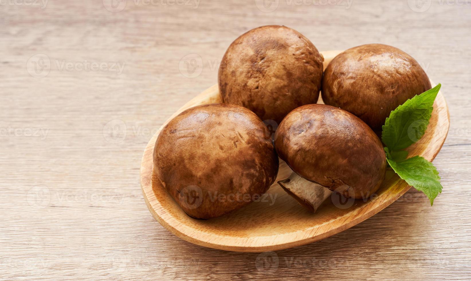 brown champignon button mushroom and green leaf in wood bowl on wooden table background. pile of brown champignon button mushroom. photo