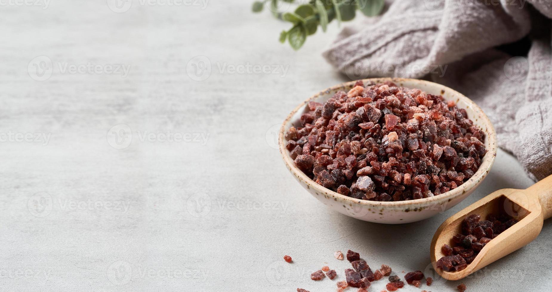 Himalayan black salt in a ceramic bowl with the wooden scoop on white cement texture background with copy space photo