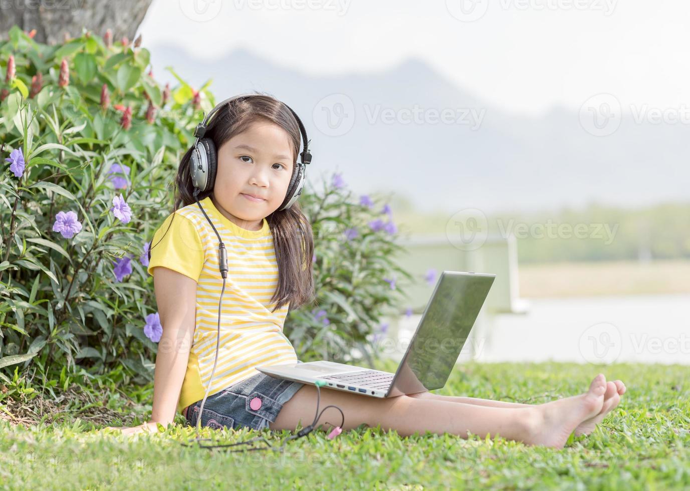 cute girl playing computer with headphone at prk. photo