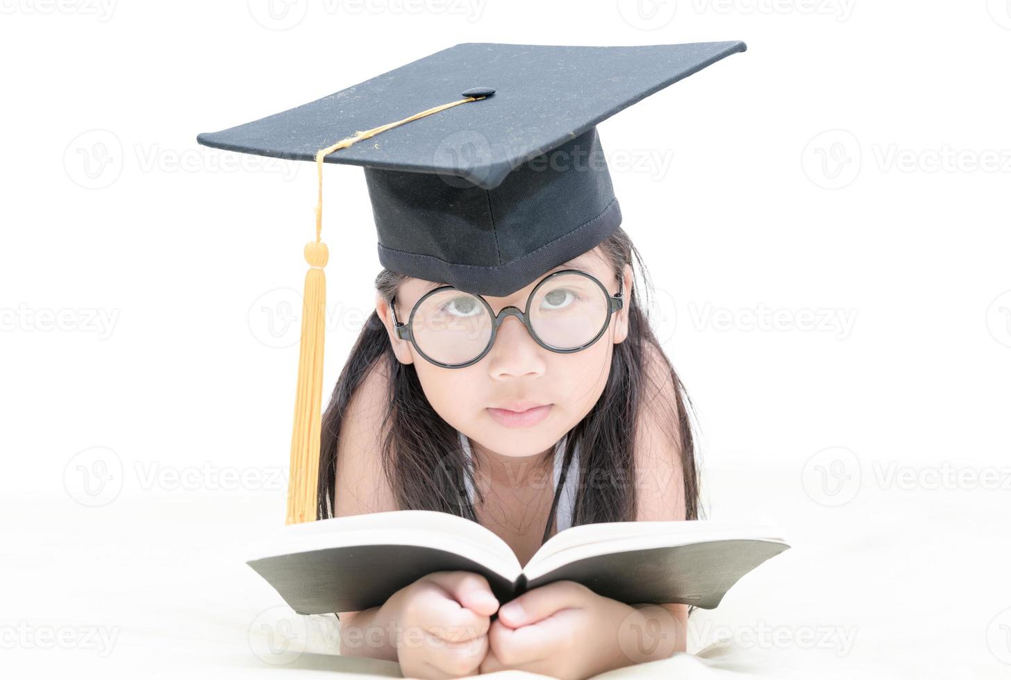 asiático colegio niño graduado leyendo libro con graduación gorra aislado foto