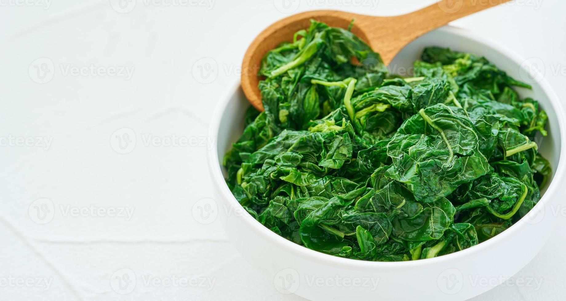 close up green cook leaf spinach salad in white bowl on white table background. leaves spinach or heap of spinach food salad photo