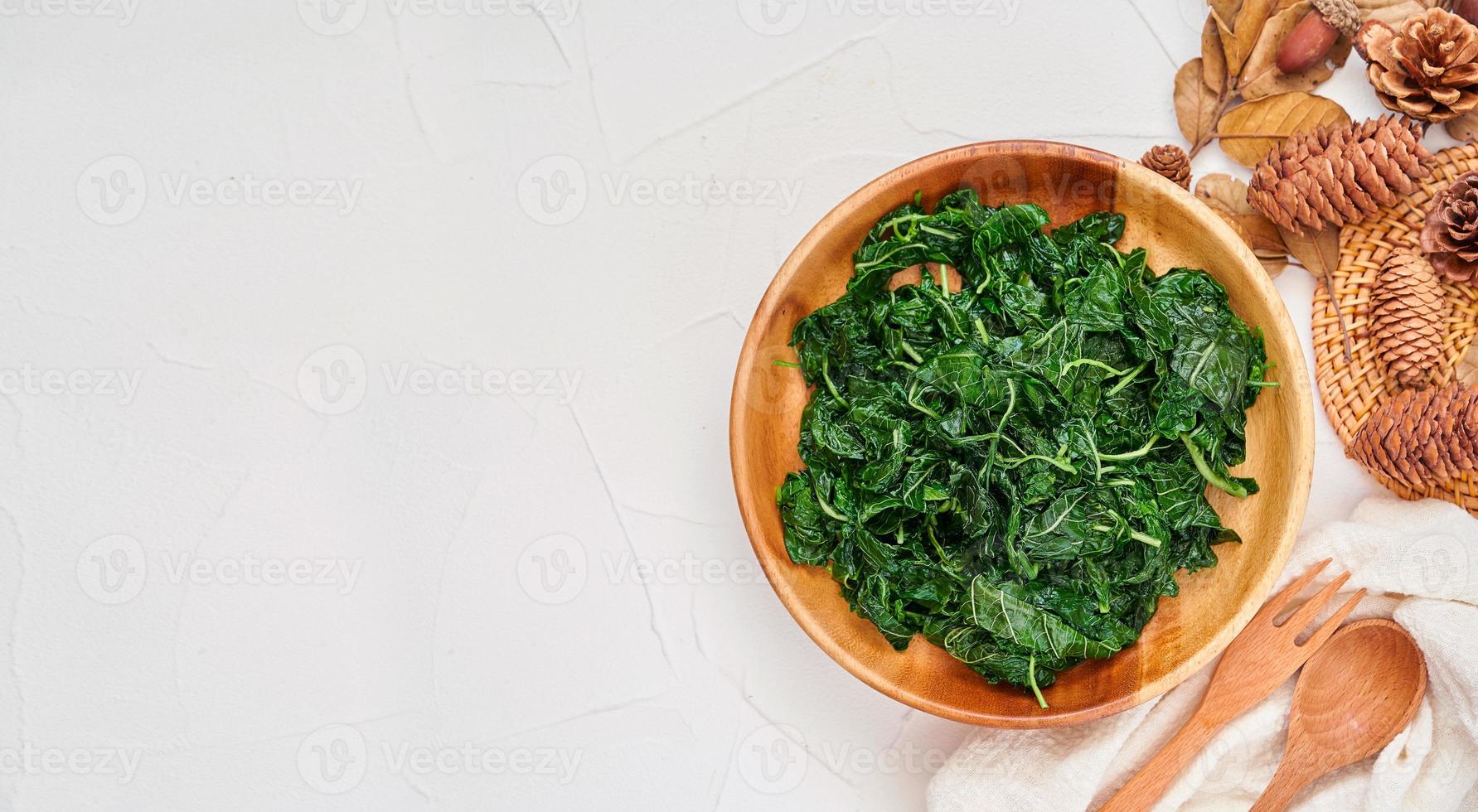 top view green cook leaf spinach salad in wood bowl on white table background. leaves spinach or heap of spinach food salad overhead, flat lay photo