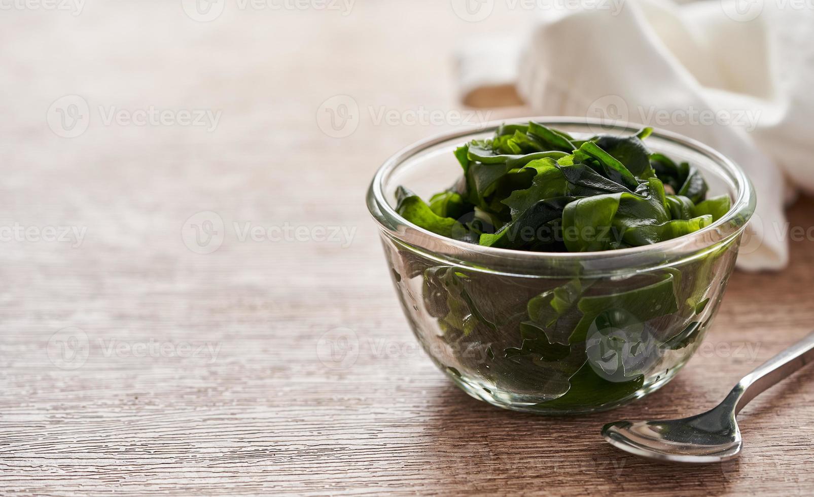 close up laminaria Kelp seaweed in glasses bowl and steel spoon on wooden table background with copy space photo