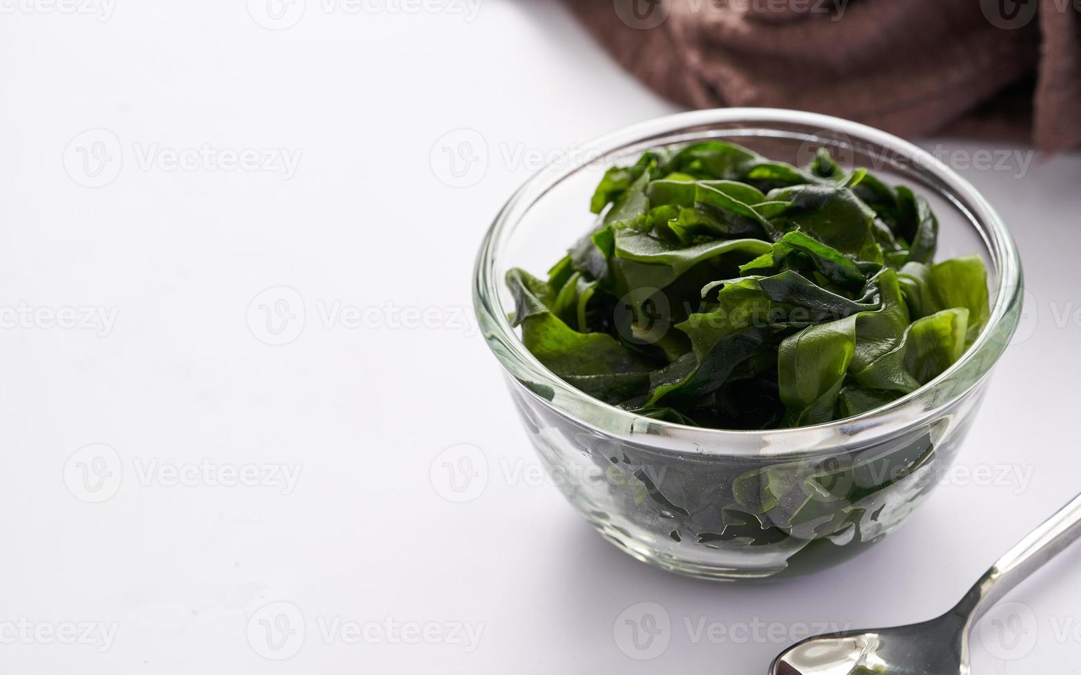 close up laminaria Kelp seaweed in glasses bowl and steel spoon on wooden table background with copy space photo