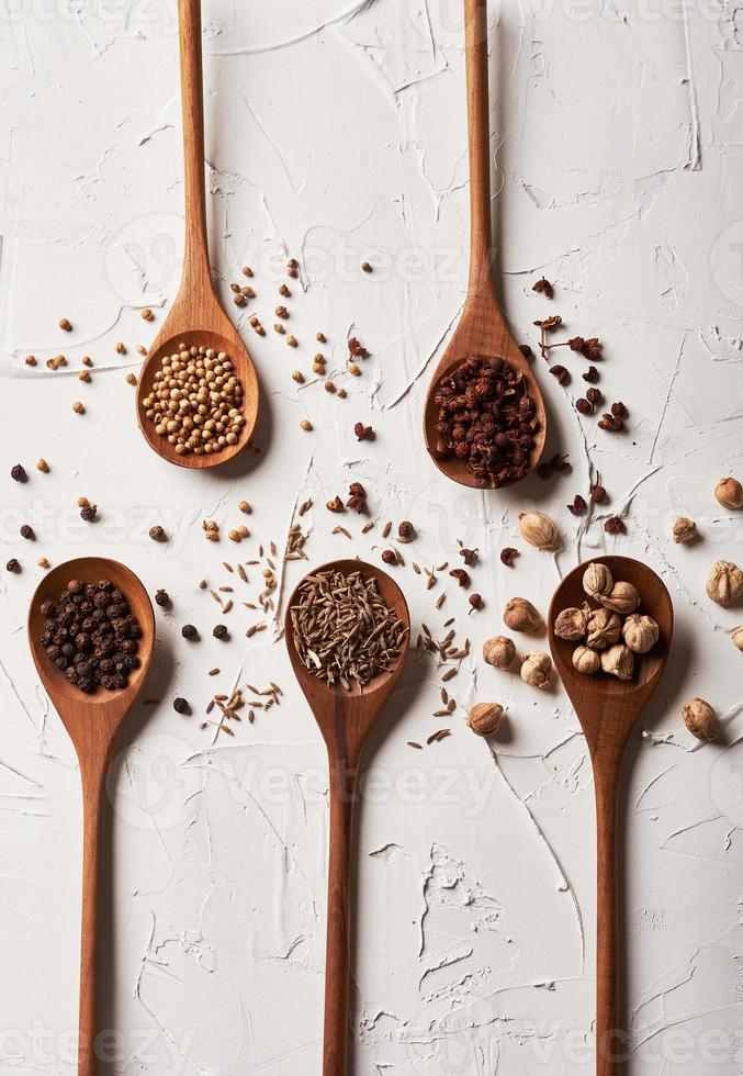 Different spices in spoon on white background. Caraway, black pepper, coriander seeds, sichuan pepper, cardamom photo