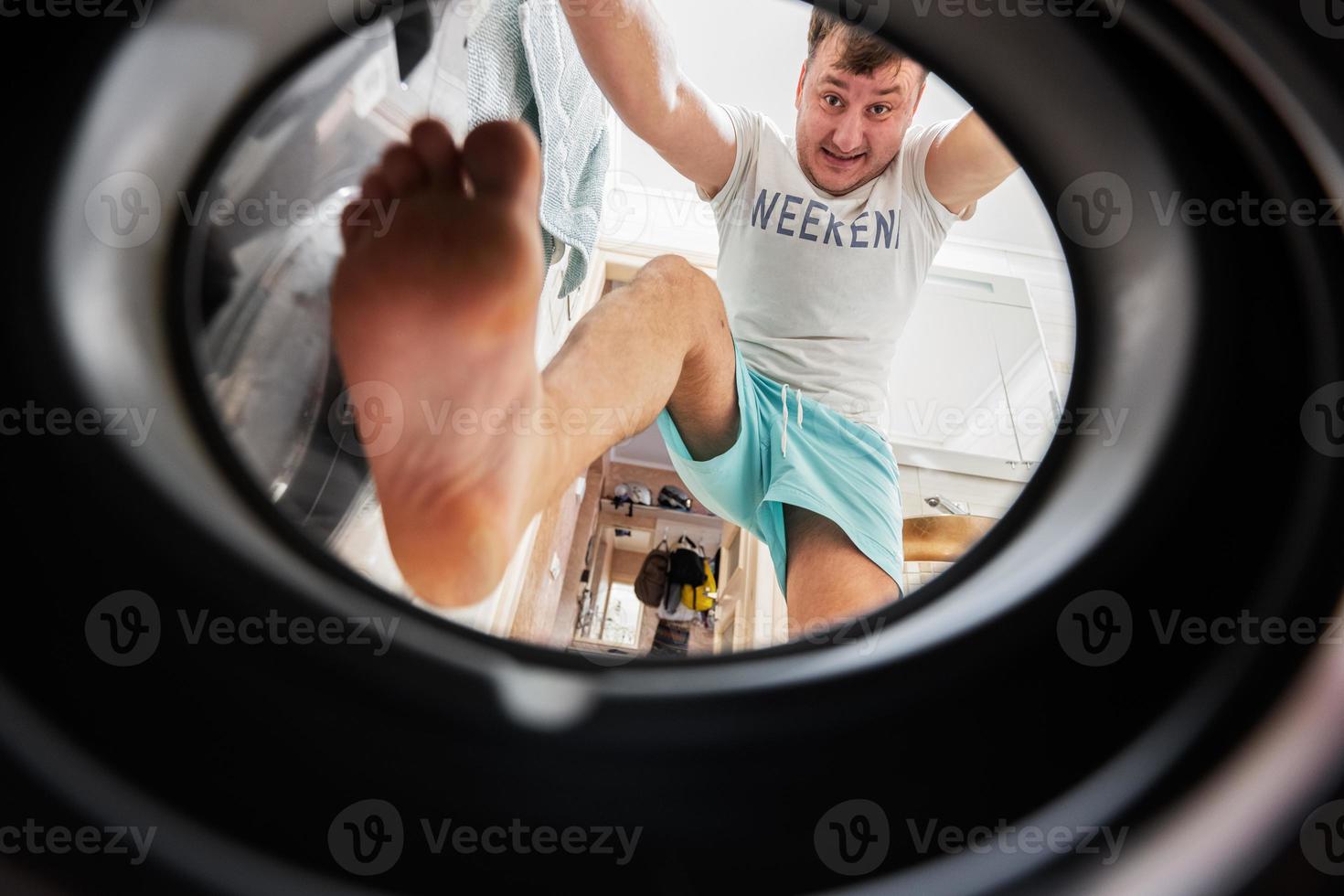 Man view from washing machine inside. Male does daily routine.  Climbs inside, pushing and pressing the laundry with his feet. photo