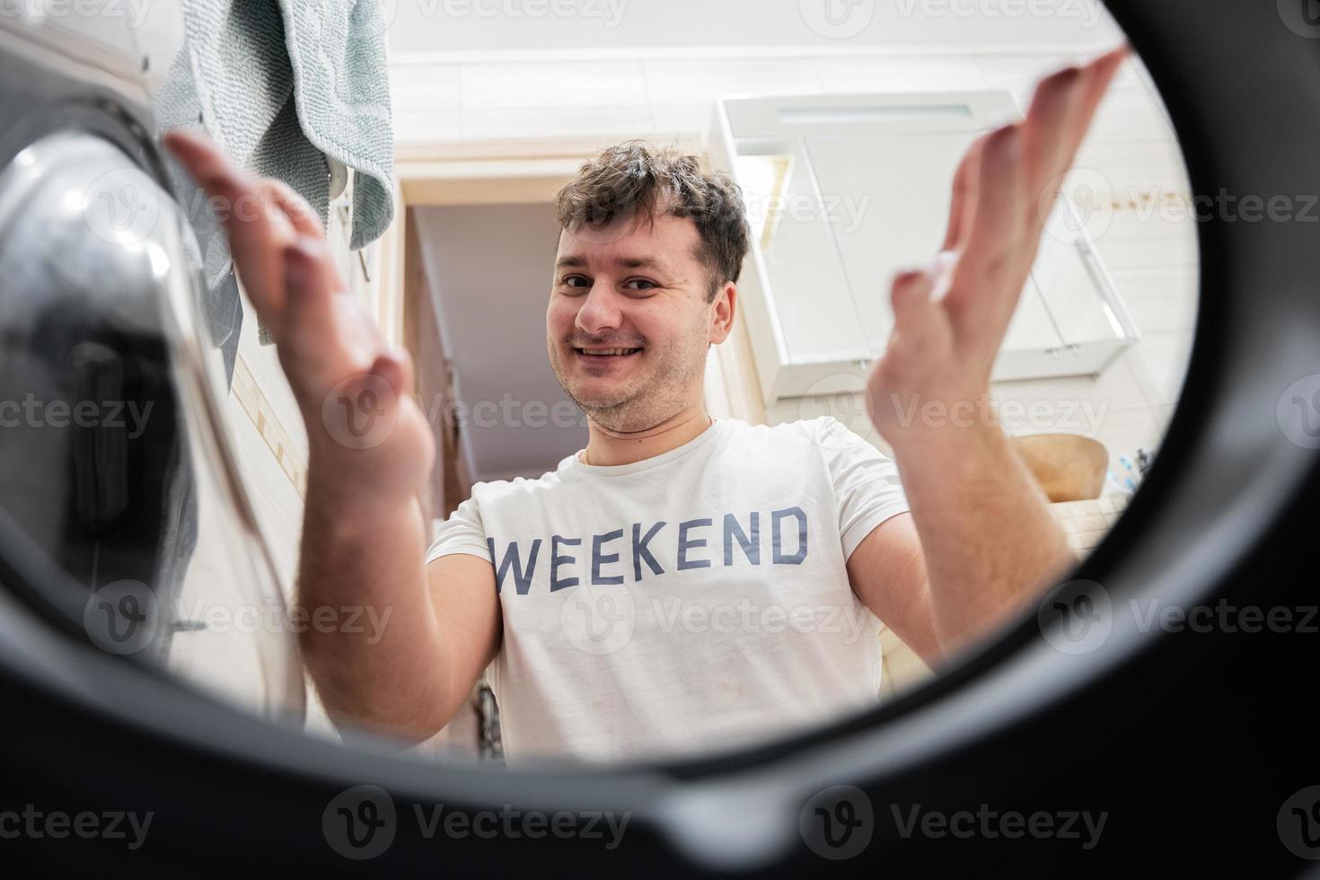 Man view from washing machine inside. Male does laundry daily routine. Satisfied expression on his face, spreading hands to the side. photo