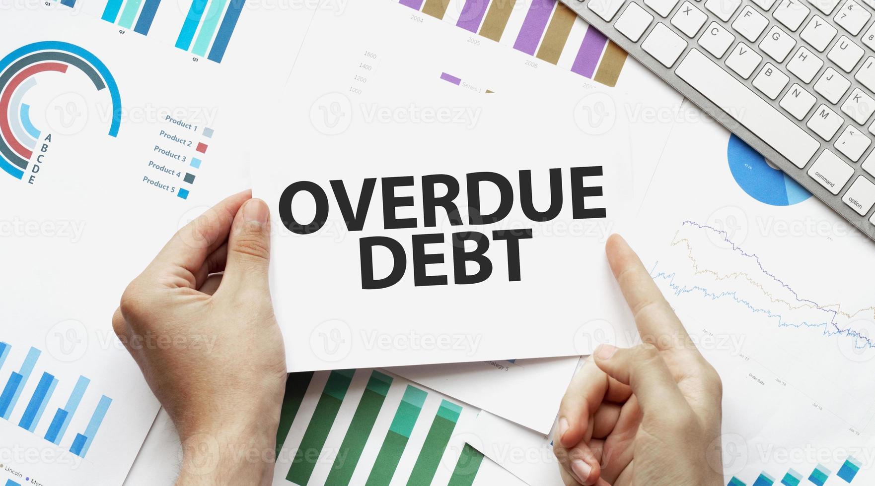 Businessman holding a card with text overdue debt .Keyboard, diagram and white background photo