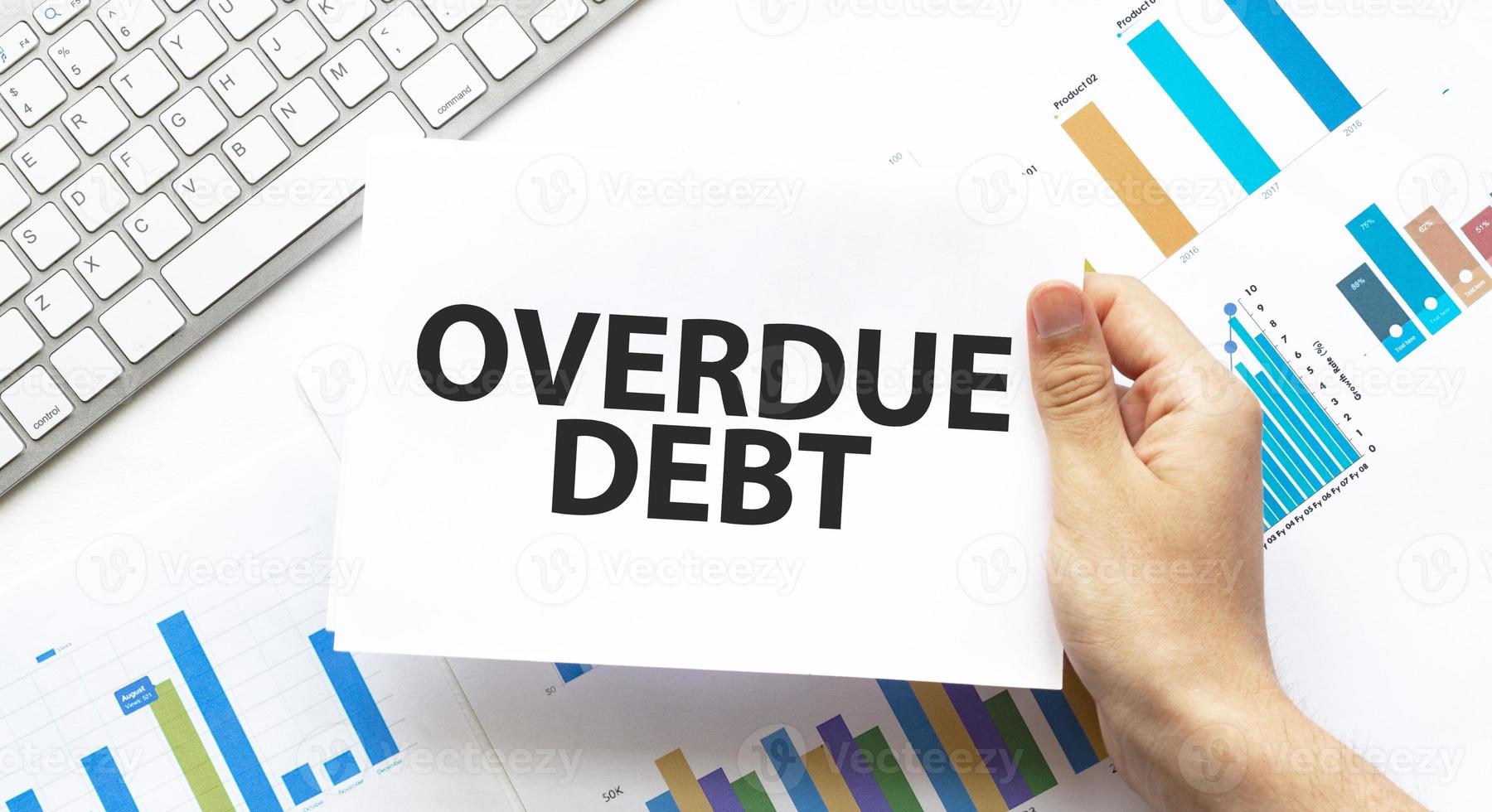 Businessman holding a card with text overdue debt .Keyboard, diagram and white background photo