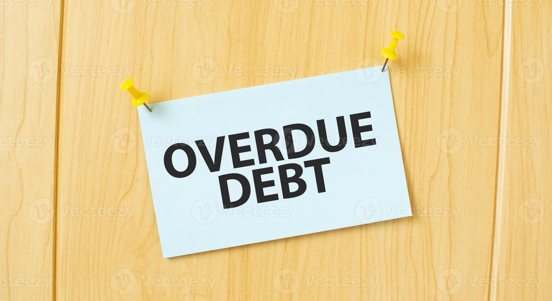 overdue debt sign written on sticky note pinned on wooden wall photo