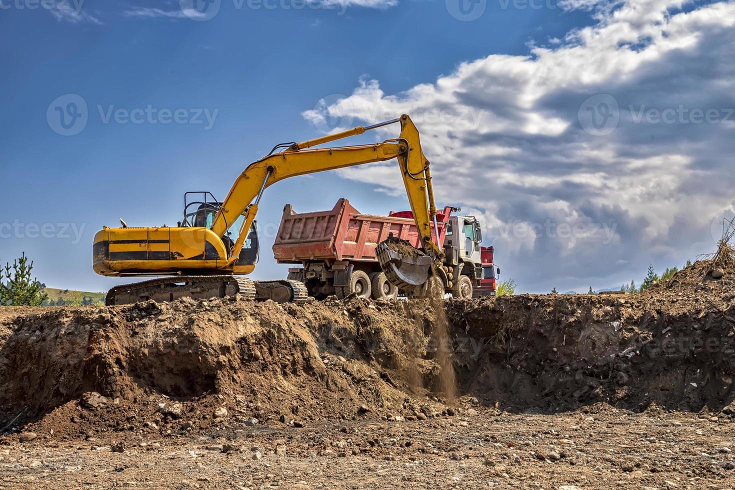 Yellow excavator and empty truck working at the construction site photo