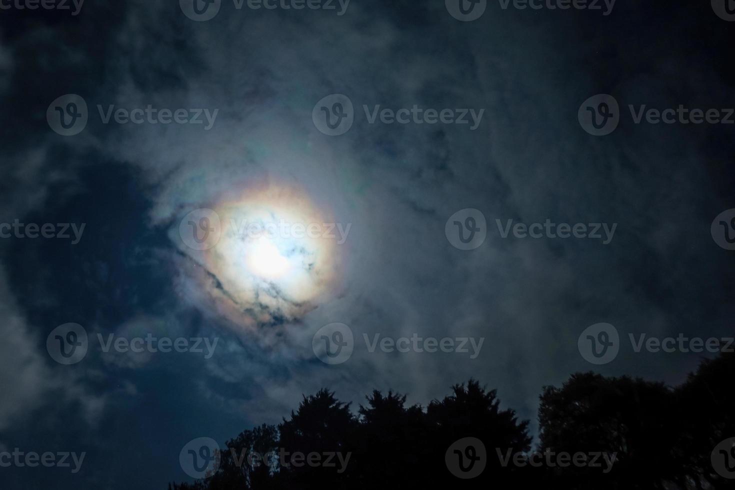 Clouds pass in front of the moon in a night sky. photo