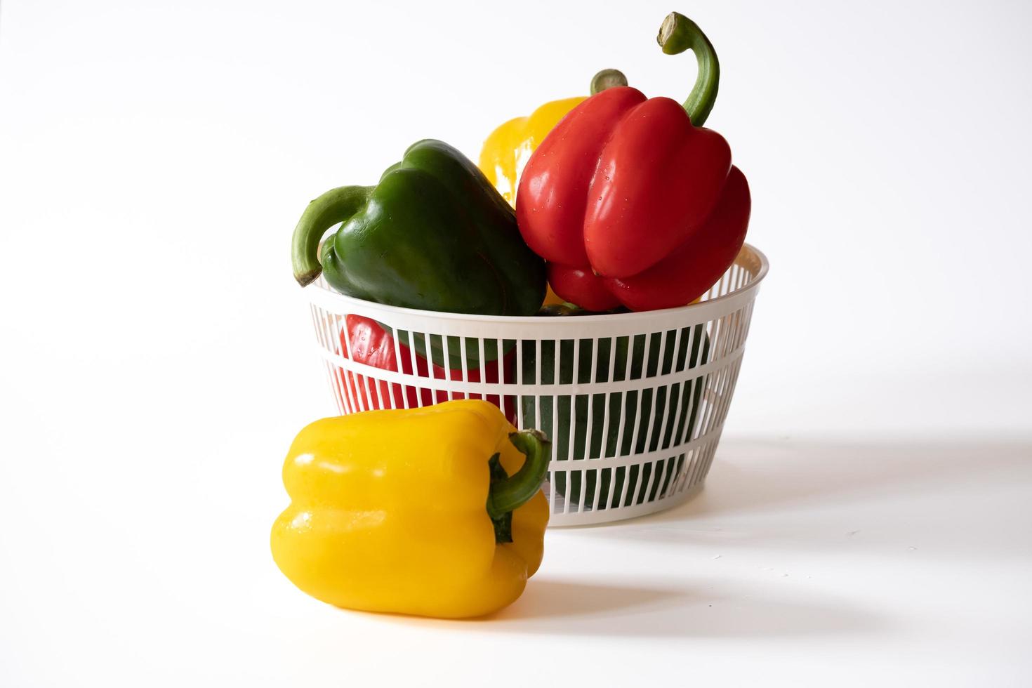 Sweet bell peppers in the white basket with water drops isolated on white background. photo